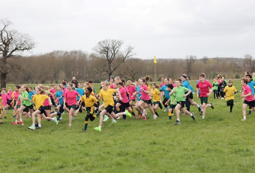 children in blue, yellow, green and pink t-shirts representing their Houses run across the Woodhall Estate for Heath Mount's annual cross country race